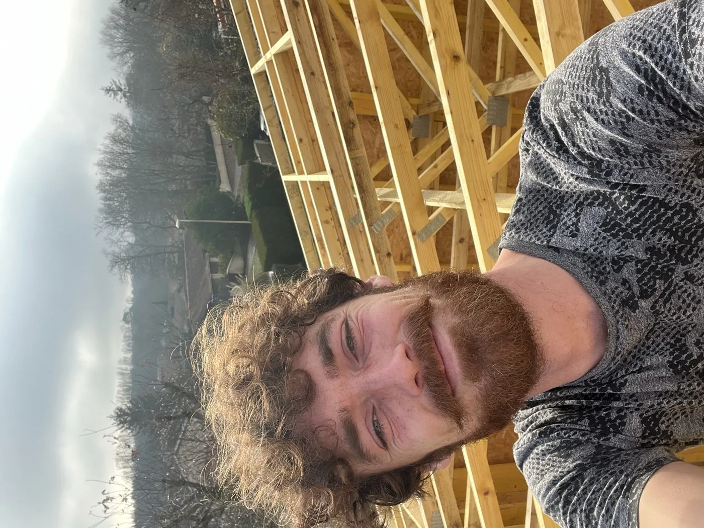 Valentin Lallemant artisan charpentier bois — souriant sur chantier avec charpente en fond